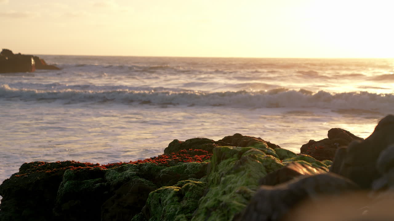 Slowmotion-video der viser havbølger ved solnedgang med tidevandsbassiner og strandelementer.