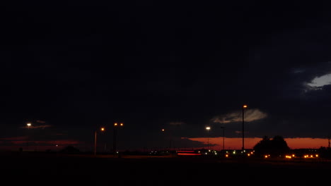 Zeitrafferaufnahme-Dramatischer-Gewitterwolken-Nach-Sonnenuntergang-Mit-Verkehr-Und-Straßenlaternen