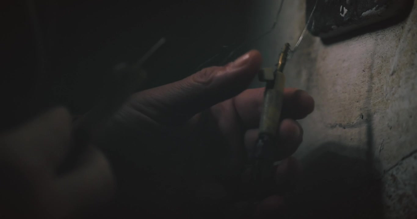 Uomo misterioso stacca i morsetti dei fili da un telefono da ingegnere vintage in un ambiente buio, evocando sorveglianza segreta, spionaggio e suspense da film noir.