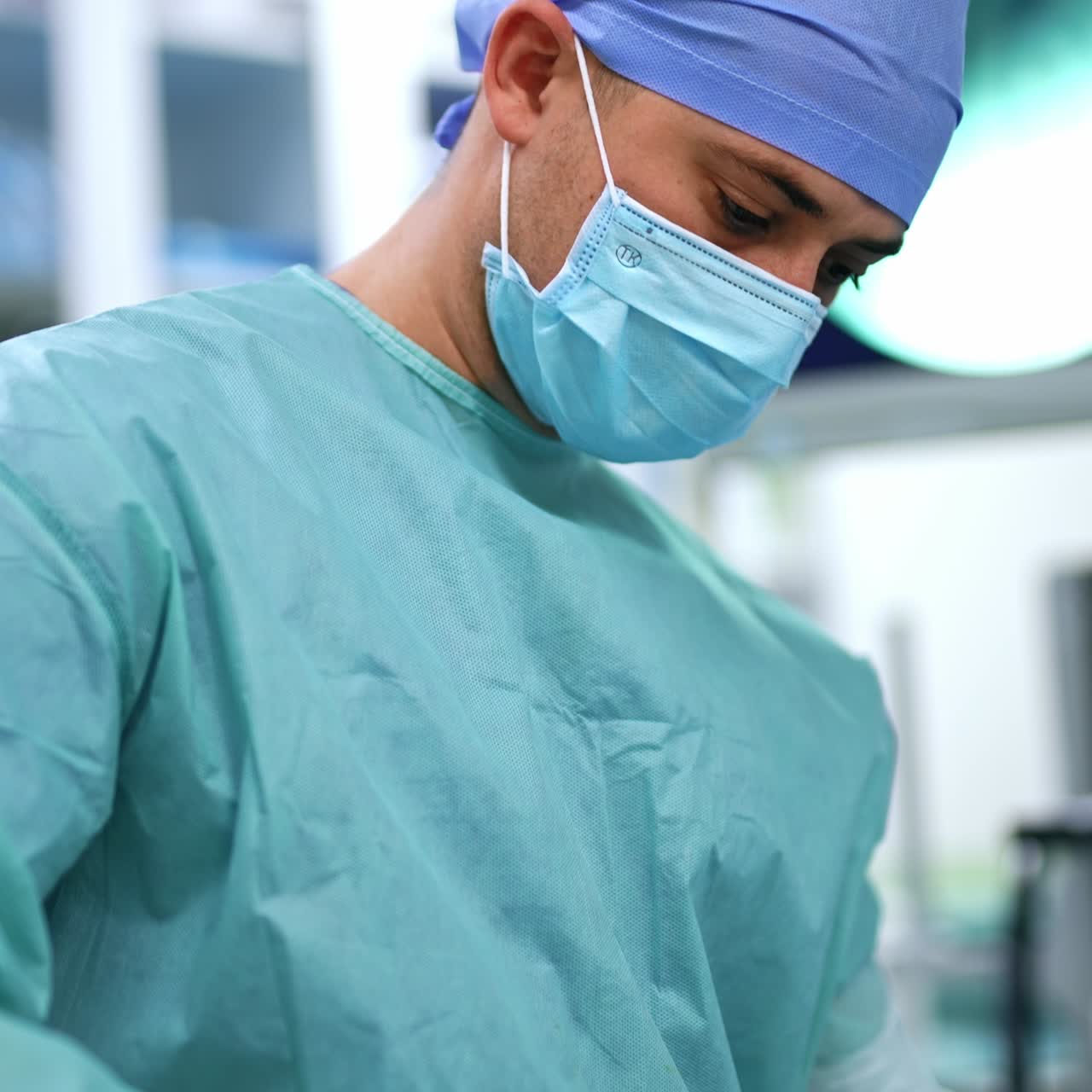 Male medical assistant holding needle and forceps to sew the patients. Blurred backdrop at modern surgery room
