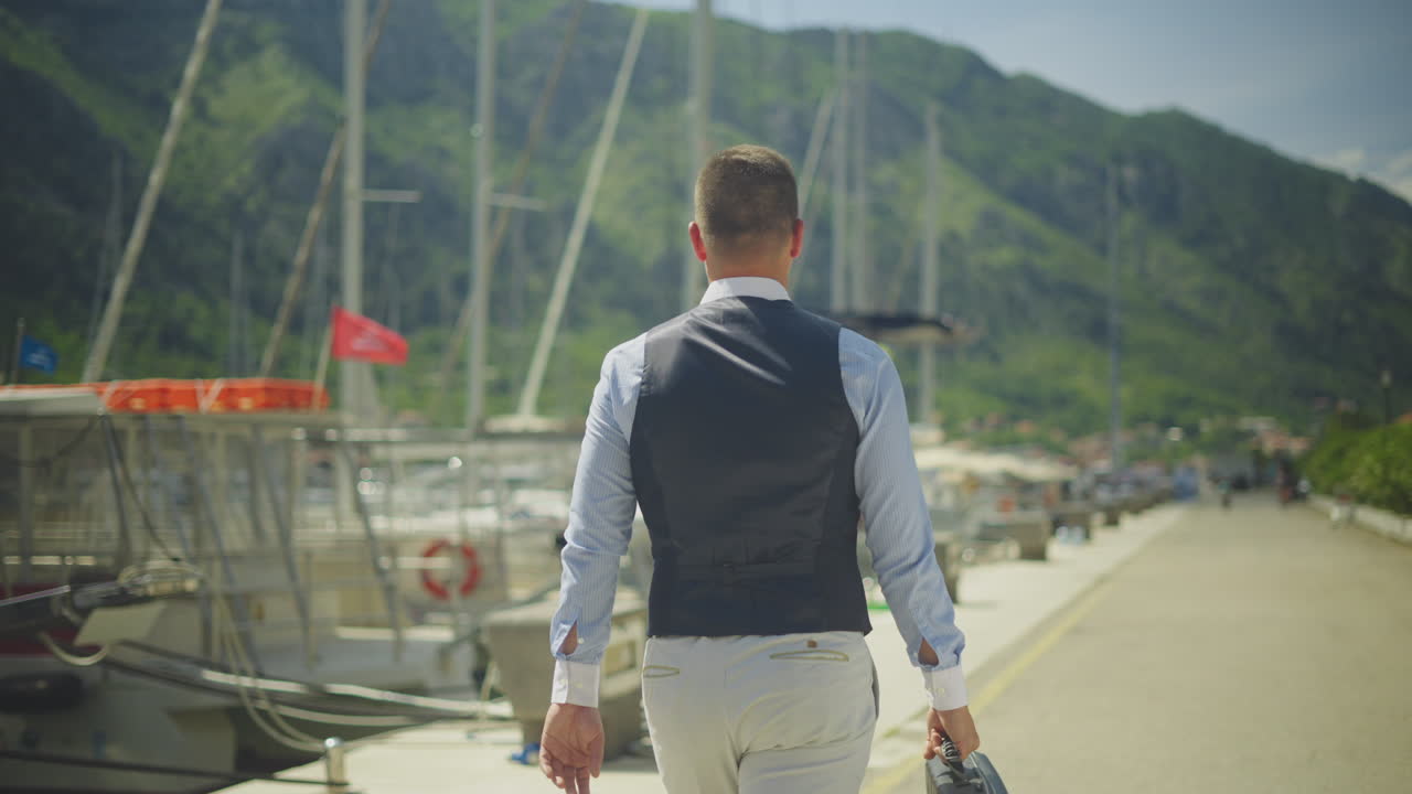 Businessman walking along the pier with a view of boats and mountains.