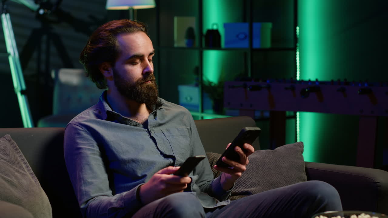 persona viendo la televisión, enviando mensajes de texto a un amigo en el teléfono móvil, sosteniendo el control remoto