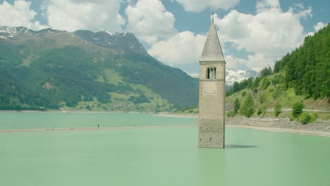 tiro completo, vista escénica de kirchturm von altgraun en el lago de reschensee en italia, gente caminando en el lecho del lago