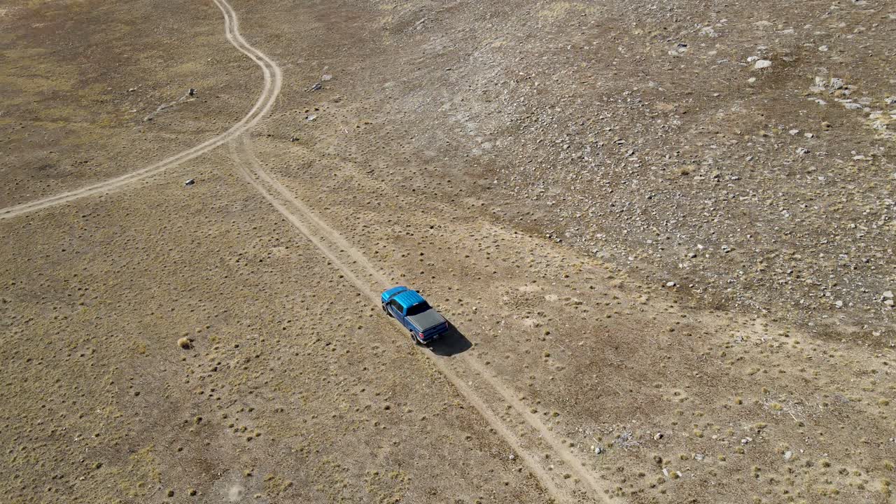 camión azul conduciendo por un camino de tierra en un árido paisaje desértico - seguimiento aéreo