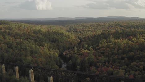 railroad trestle in the forest crossing a winding stream with early fall foliage at sunset aerial reveal