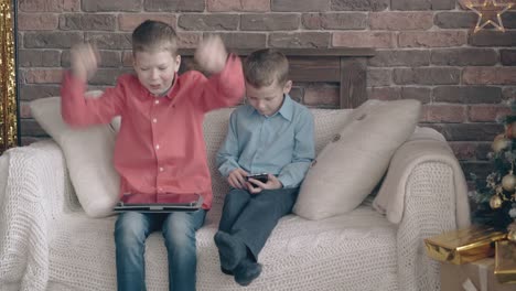 brothers-sit-on-sofa-playing-on-tablet-and-smartphone