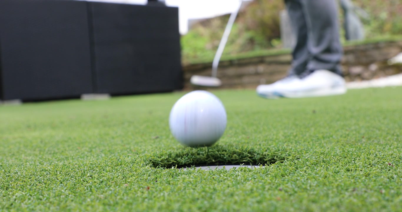 Golf Putting - putting stroke with first attempt missing the whole, second attempt into the hole. Close up of hand retrieving the golf ball.