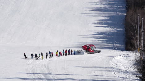 red snow groomer turning right towing a group of skiers,snowy hill