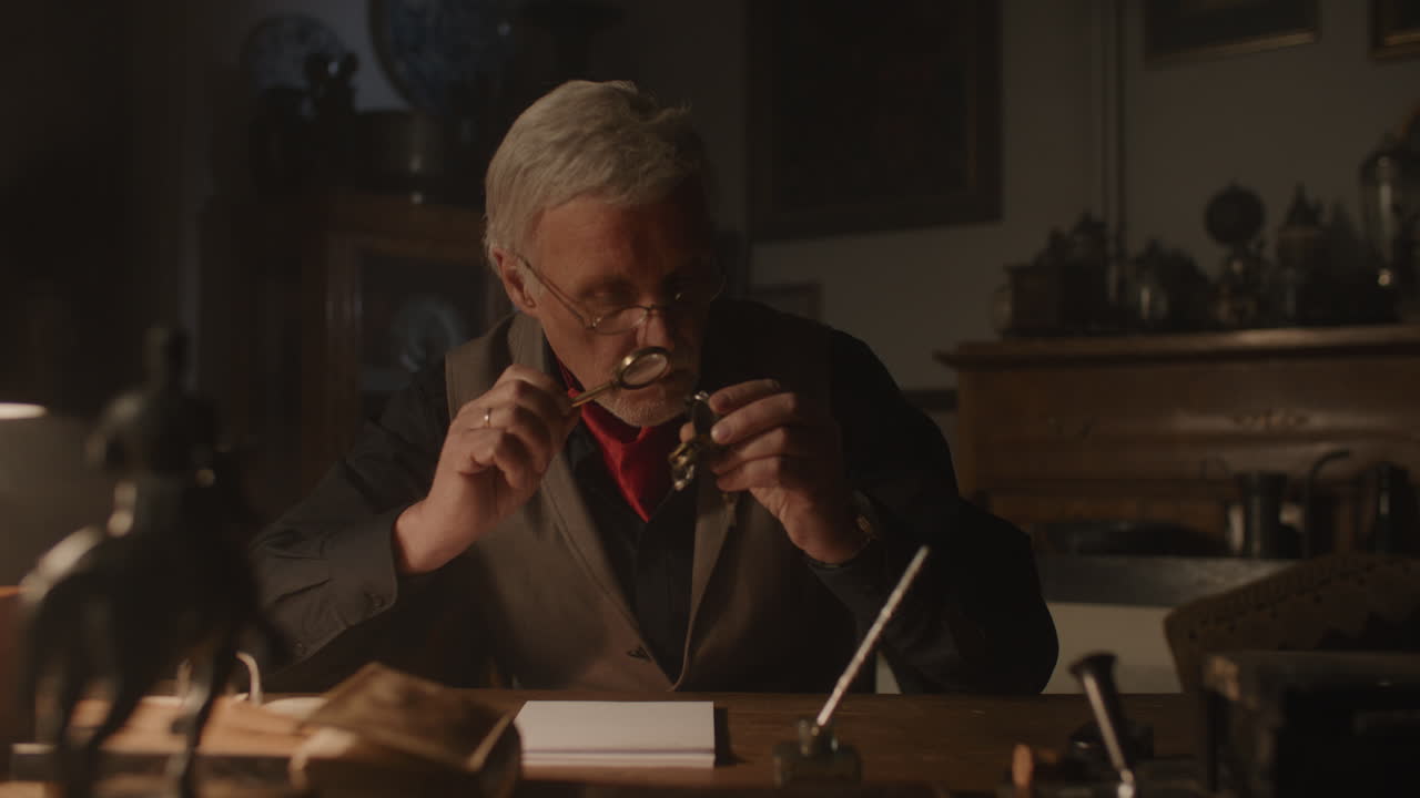 Older passionate man evaluates an old silver skull watch in his office at night