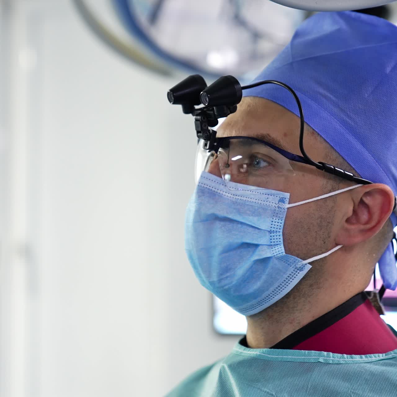 Male surgeon talking during operation. Neurosurgeon wearing mask and special glasses with technical device on. Close up