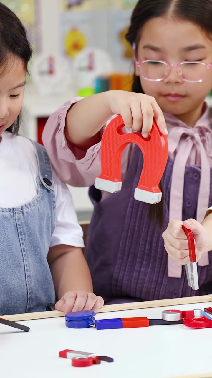Dua gadis muda menggunakan magnet tapal kuda untuk belajar fisika di ruang kelas yang terang