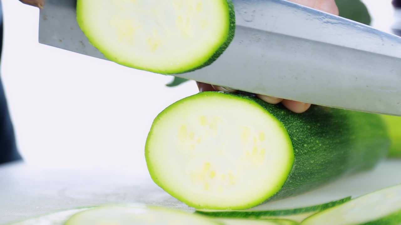 4k 여성 손으로 는 보드에 신선한 zucchini를 자르고 여성 손으로 자르는 보드에 칼로 원시 일본 호박을 원형으로 잘라 건강한 음식 개념.
