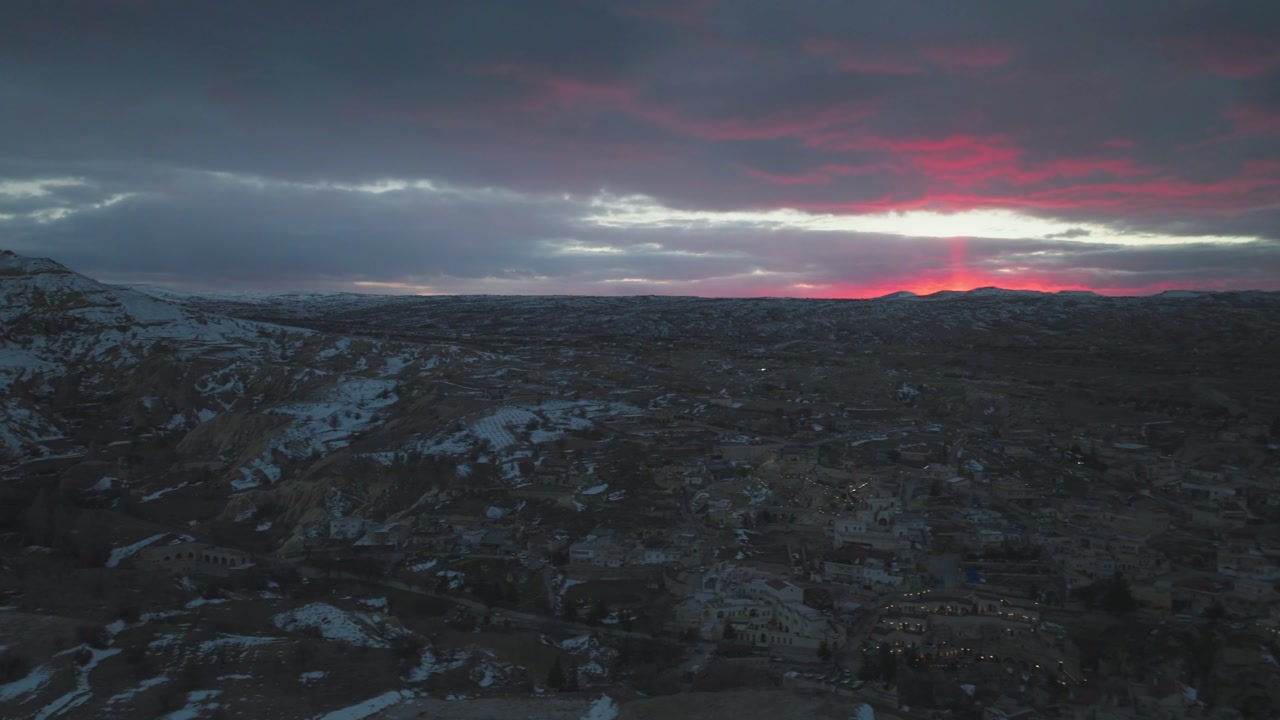 Mustafapasa aerial drone in cappadocia, Turkey capturing a vast mountain range partially covered in snow under a vibrant red and purple sunset sky. Turkiye, Turkey