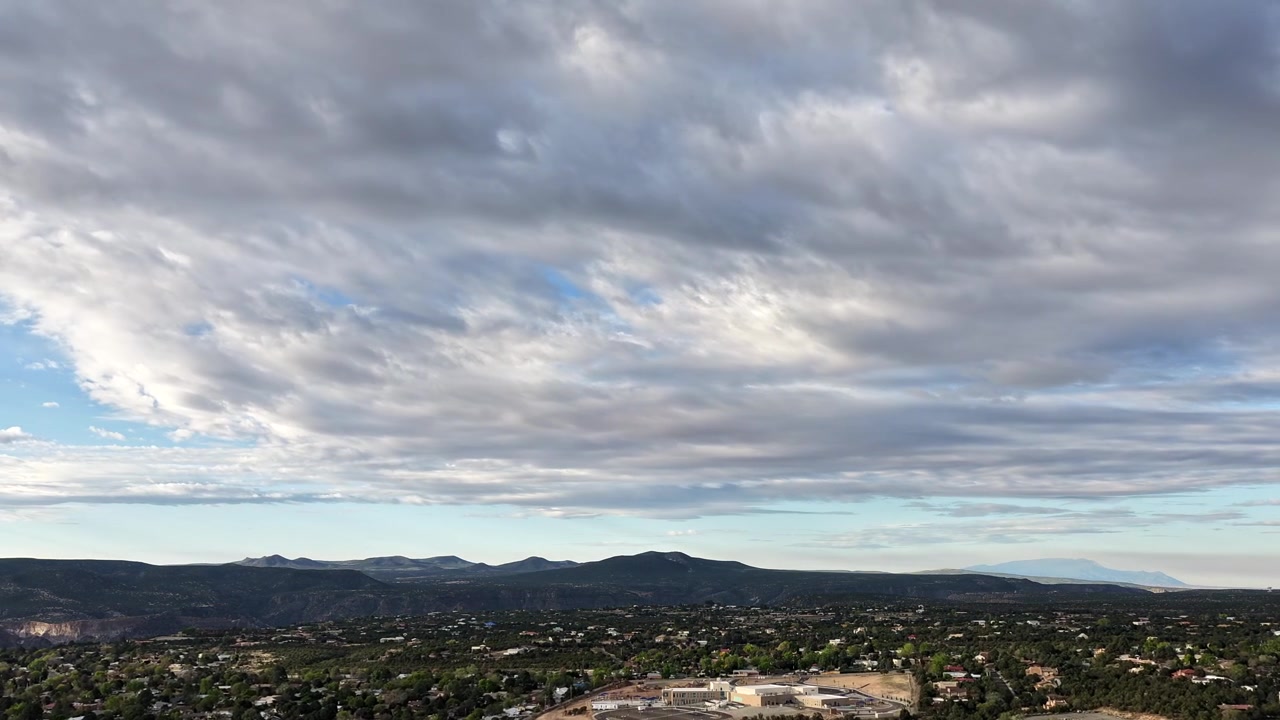 A cinematic 4K drone timelapse captures rolling clouds and atmospheric motion over a southwest mountain town. The shifting light and rapid cloud movement create an epic nature background for B-roll.