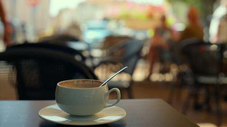 Empty coffee cup with a spoon resting on a table at an outdoor cafe, people blurred in background enjoying the atmosphere