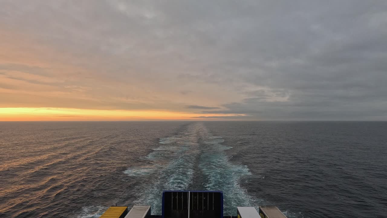 Kielwasser einer Transportfähre, die an einem grauen, bedeckten Tag fährt, goldener Horizont