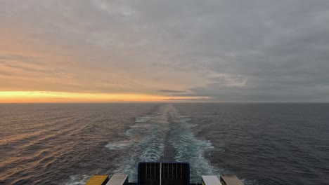 wake of transport ferry sailing on grey overcast day, golden horizon