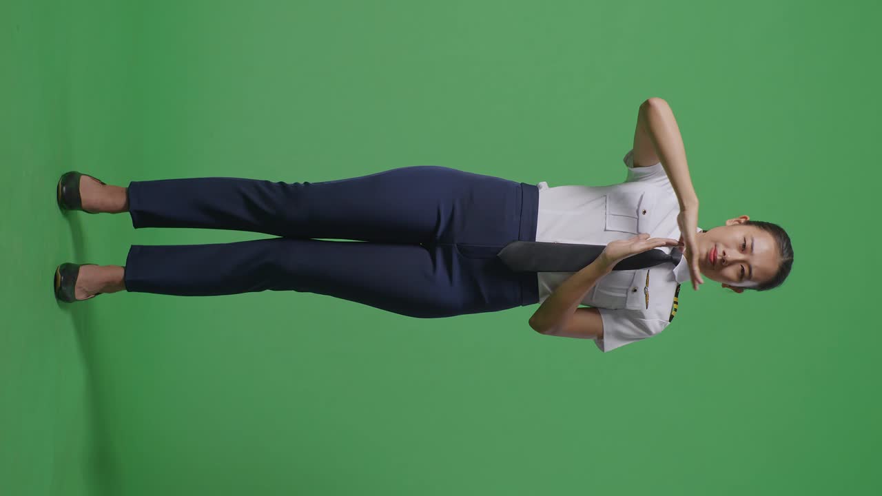 아시아 여성 조종사가 카메라를 바라보며 시간을 보여주는 몸매가 녹색 스크린 배경 스튜디오에 서 있는 동안