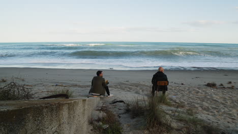father and son watch the ocean waves crash while sitting on the beach