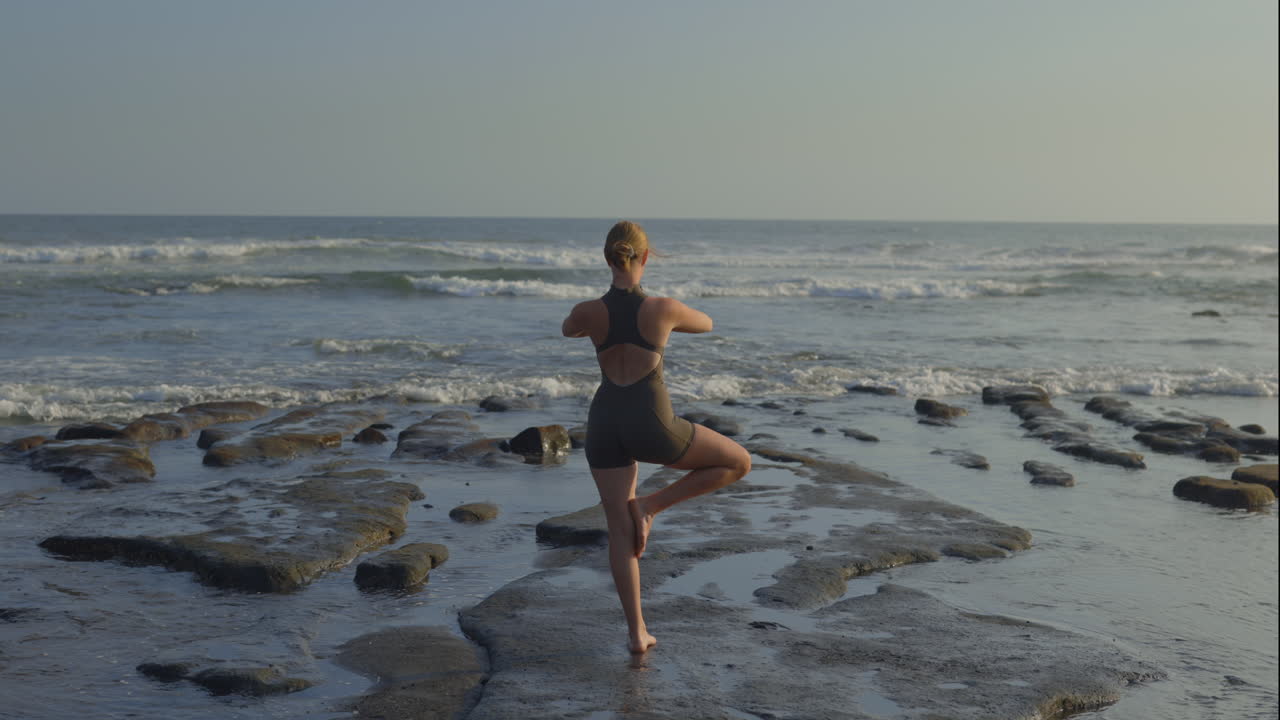 Donna che fa yoga su una spiaggia rocciosa