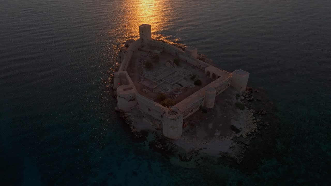 Middelalderborg badet i gyllent morgengrylys over det fredfylte Middelhavet