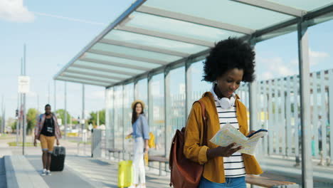 joven viajera afroamericana con mochila sosteniendo un mapa de la ciudad mientras camina en la estación de autobuses