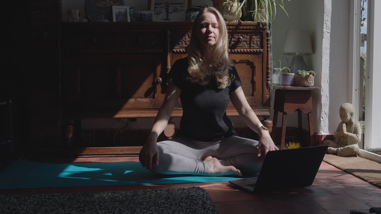 Woman doing yoga in a living room with a laptop