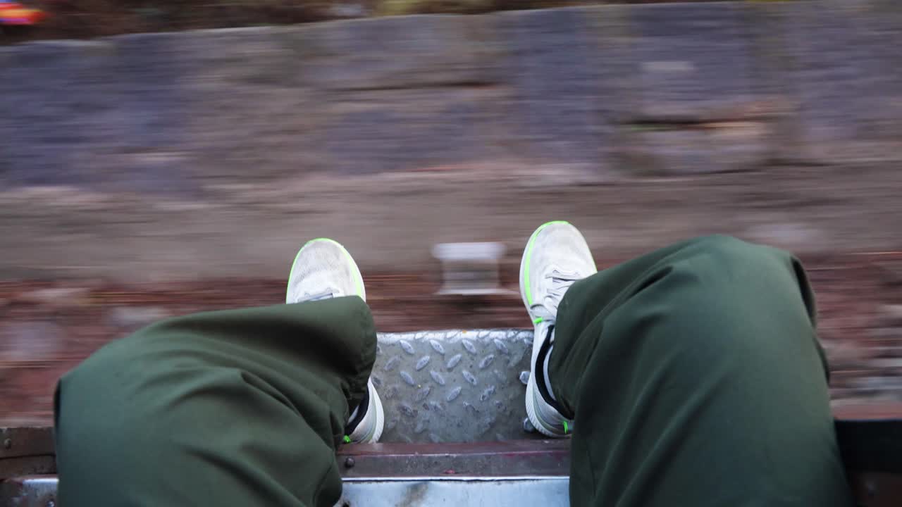 person sitting at train doorway with legs outside moving railway track motion blur travel scene