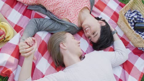 Overhead-view-of-caucasian-lesbian-couple-lying-on-the-blanket-in-the-garden-during-picnic