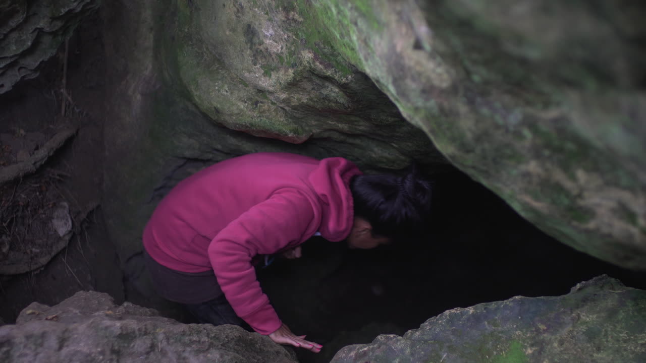 A woman wearing a pink sweater stumbles upon a secluded cave on Te Waewae Island in New Zealand