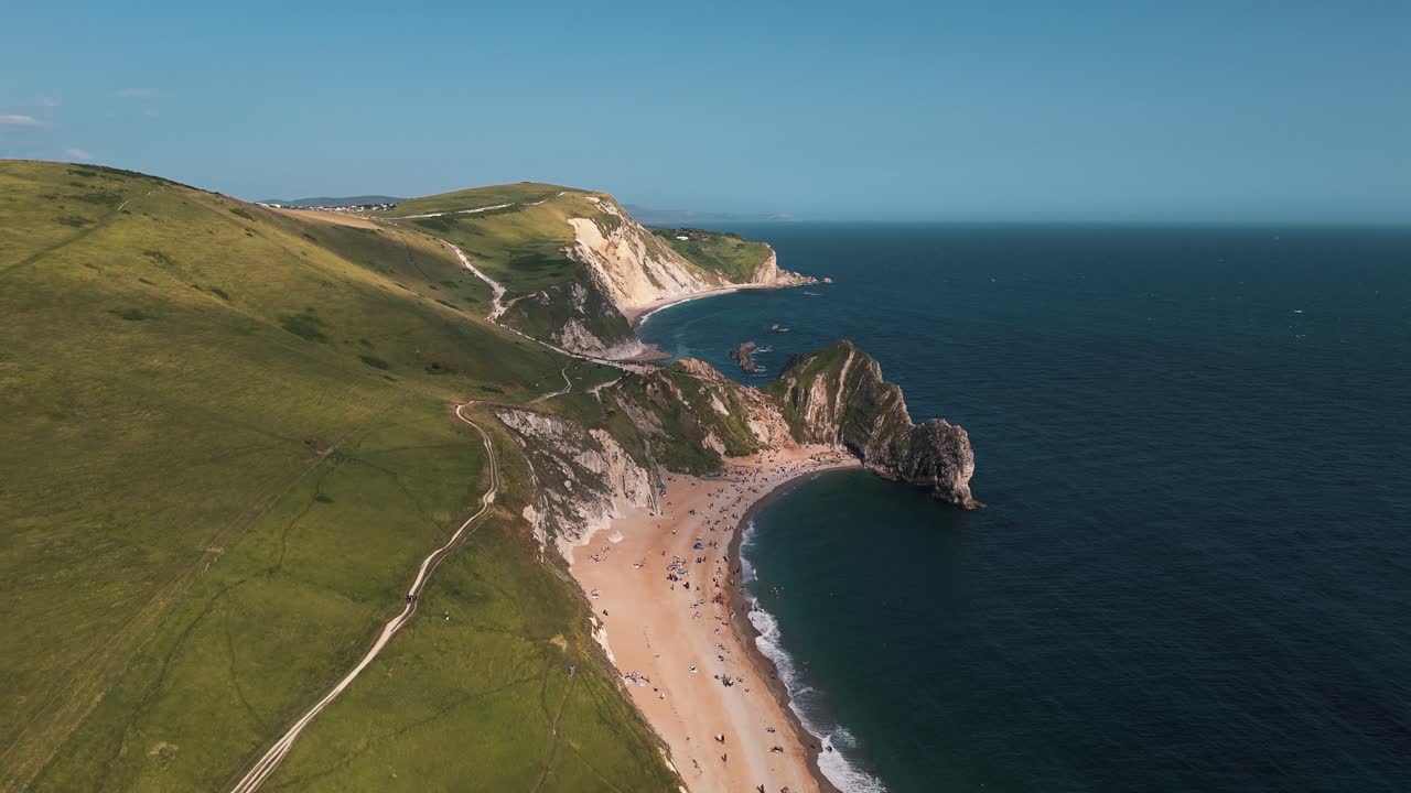 High drone retreat from Durdle Door showing entire archway and coastline in afternoon light, establishing aerial