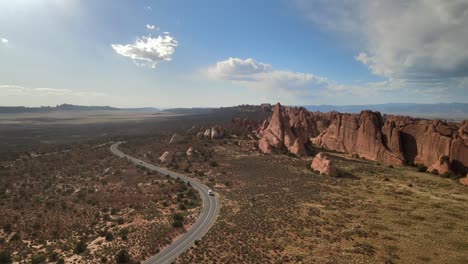 A-panoramic-aerial-view-of-Arches-National-Park,-featuring-a-meandering-road-in-the-center-with-cars-traveling-along-it