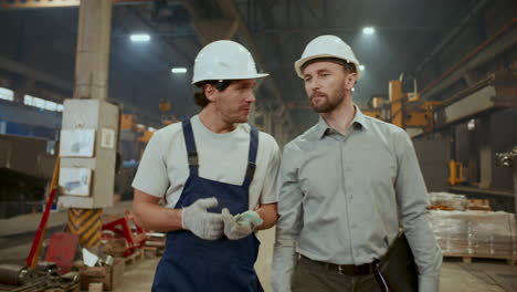 worker and engineer walking through factory, discussing manufacturing process