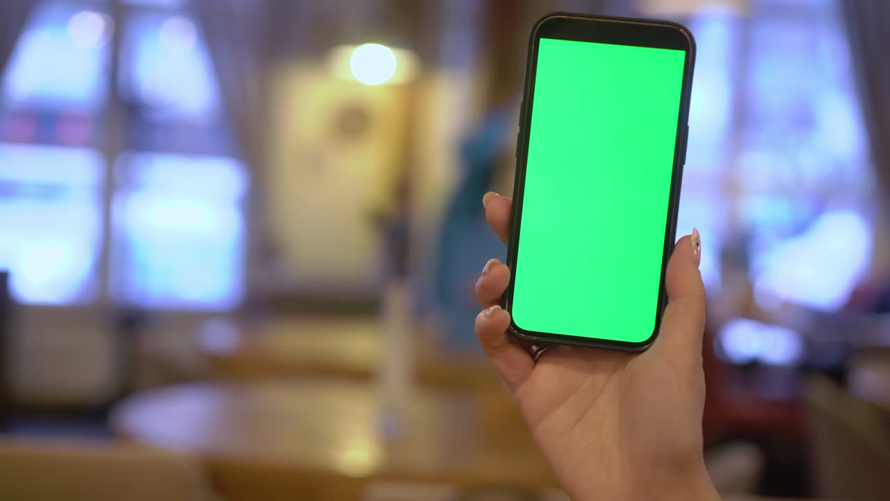 A woman holds a mobile phone in her hand with a green chromakey screen
