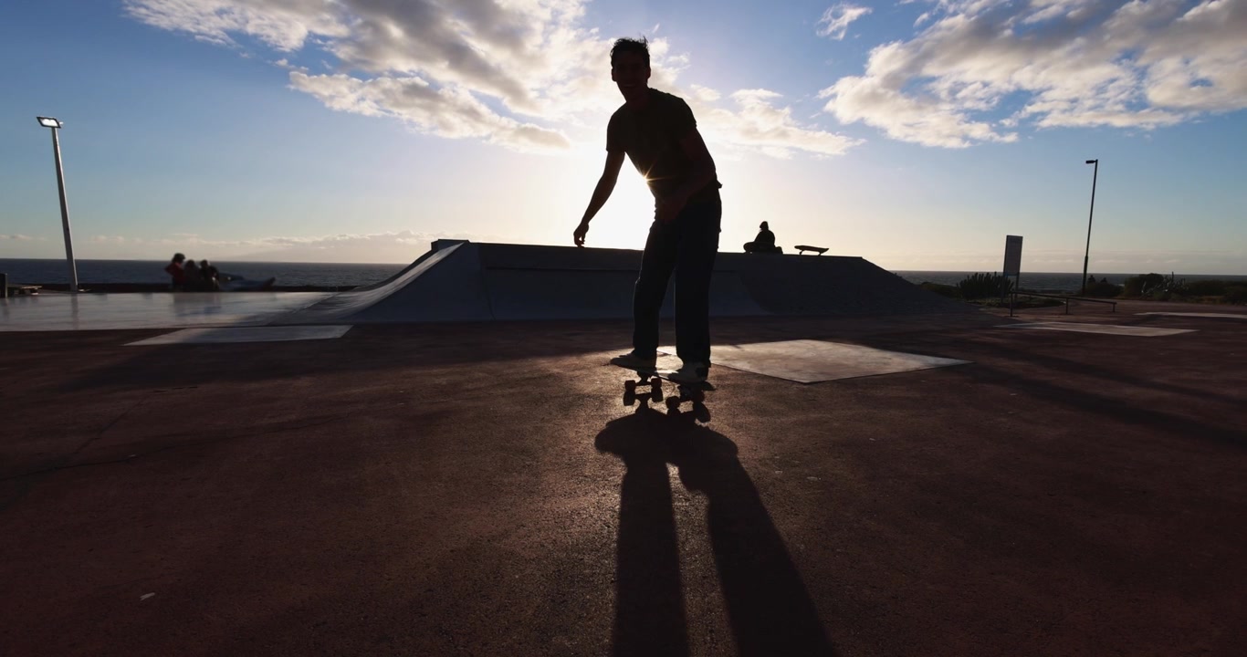 Skateboarder i silhuet mod solnedgangshimlen i en kystnær skatepark
