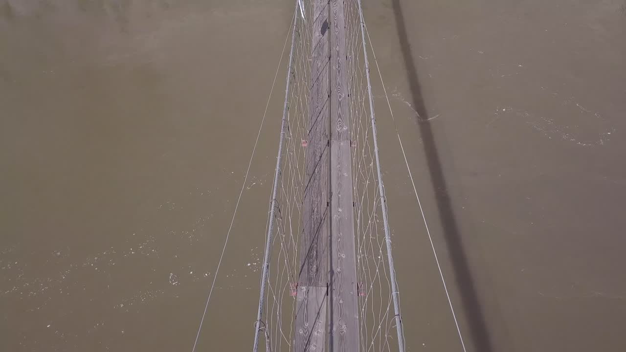 Muddy river swirls below intimidating, narrow suspension foot bridge