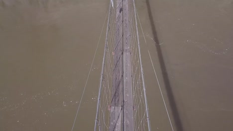 muddy river swirls below intimidating, narrow suspension foot bridge