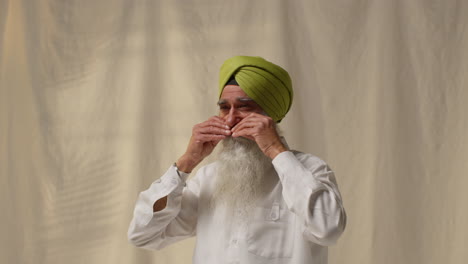 fotografía de estudio de un anciano sikh arreglando la barba y el bigote comprobando el turbante contra un fondo plano