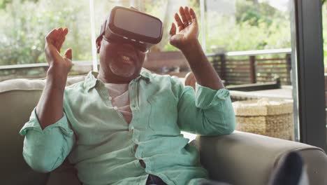 행복 한 아프리카계 미국인 노인 이 거실 에 앉아 vr 헤드 ⁇  을 사용 하고 미소 짓고 있다