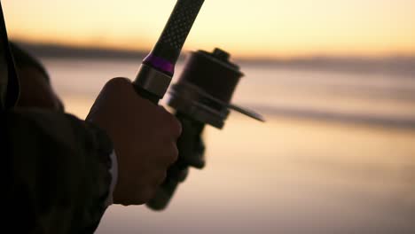 handle rotation with reel of fishing rod against of orange sunset slow motion