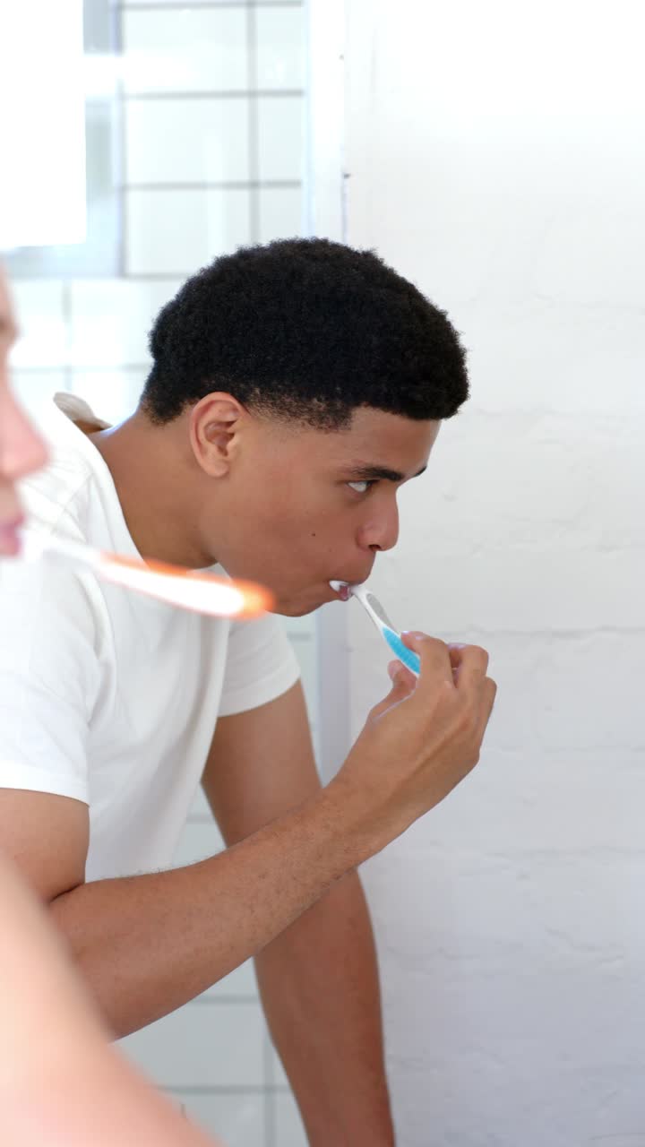 Vertical video: Diverse couple brushing at sink for oral care, man leaning while brushing with foam