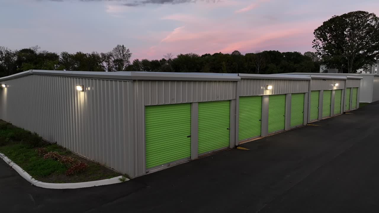 Green colored garages and rental self storage units in American suburb. Dusk scene in fall season. Lights on metal facade of garages. Aerial close up