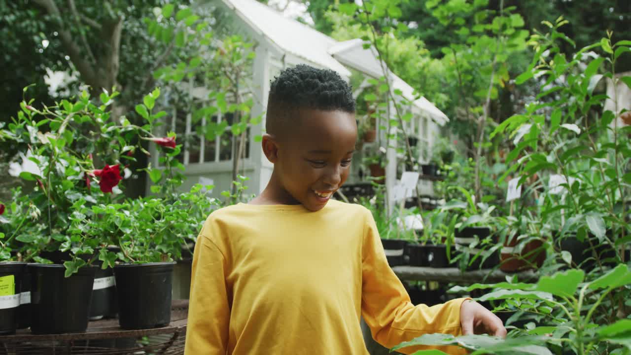 retrato de un feliz niño afroamericano mirando plantas y sonriendo en el jardín