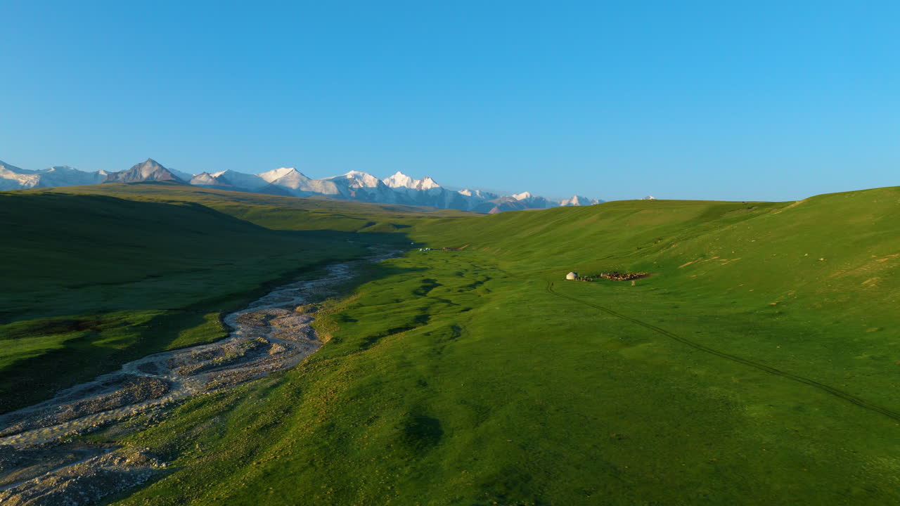 Dolci colline verdi e un alveo tortuoso nella Valle di Sary Jaz in Kirghizistan, con le montagne Tian Shan in lontananza. Ampia ripresa con drone.