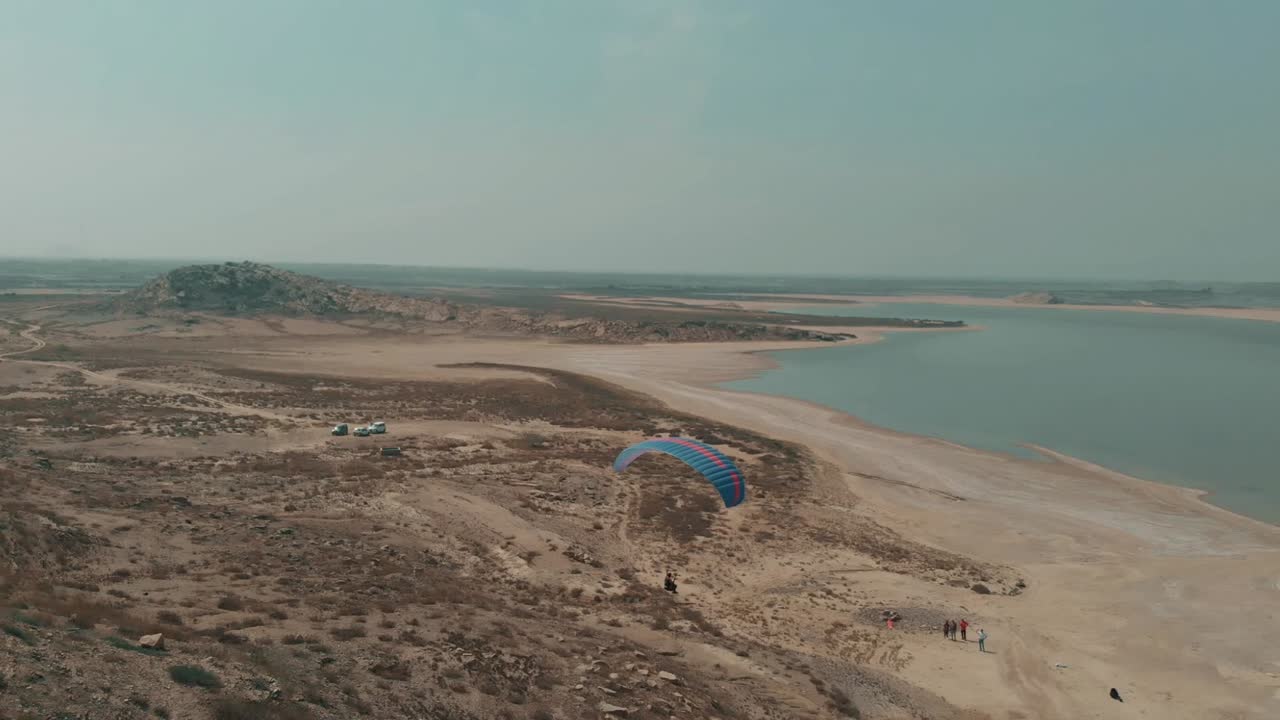 toma aérea de un parapente aterrizando junto al lago salado en karachi