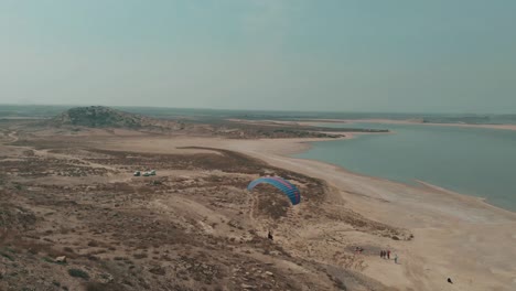 Toma-Aérea-De-Un-Parapente-Aterrizando-Junto-Al-Lago-Salado-En-Karachi