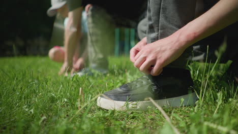 close-up leg view of three people adjusting their shoelaces while squatting on a grassy field with a blur background