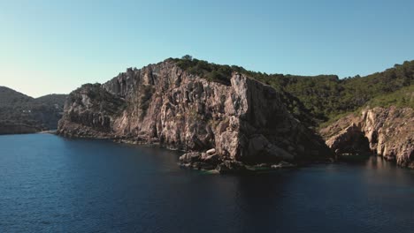 Drone-shot-steep-tall-cliffs-on-coast-of-island-with-ocean-water-below