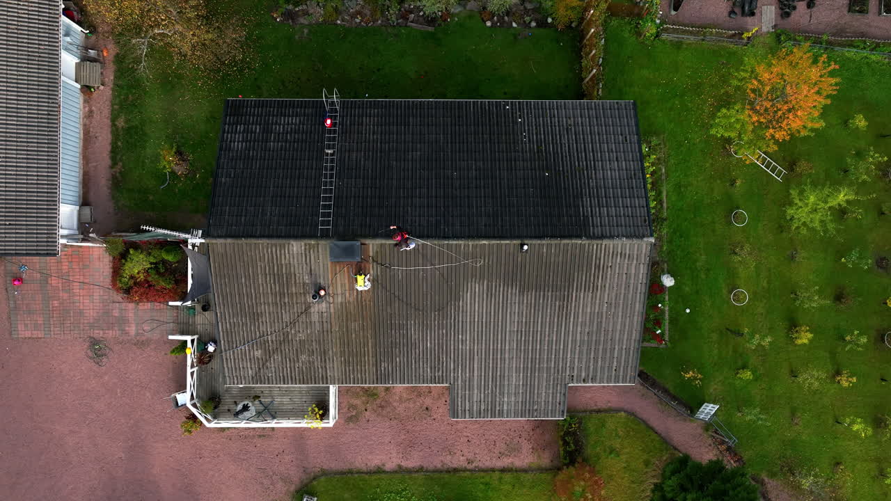 Birdseye drone shot above a woman pressure washing a house roof, autumn day