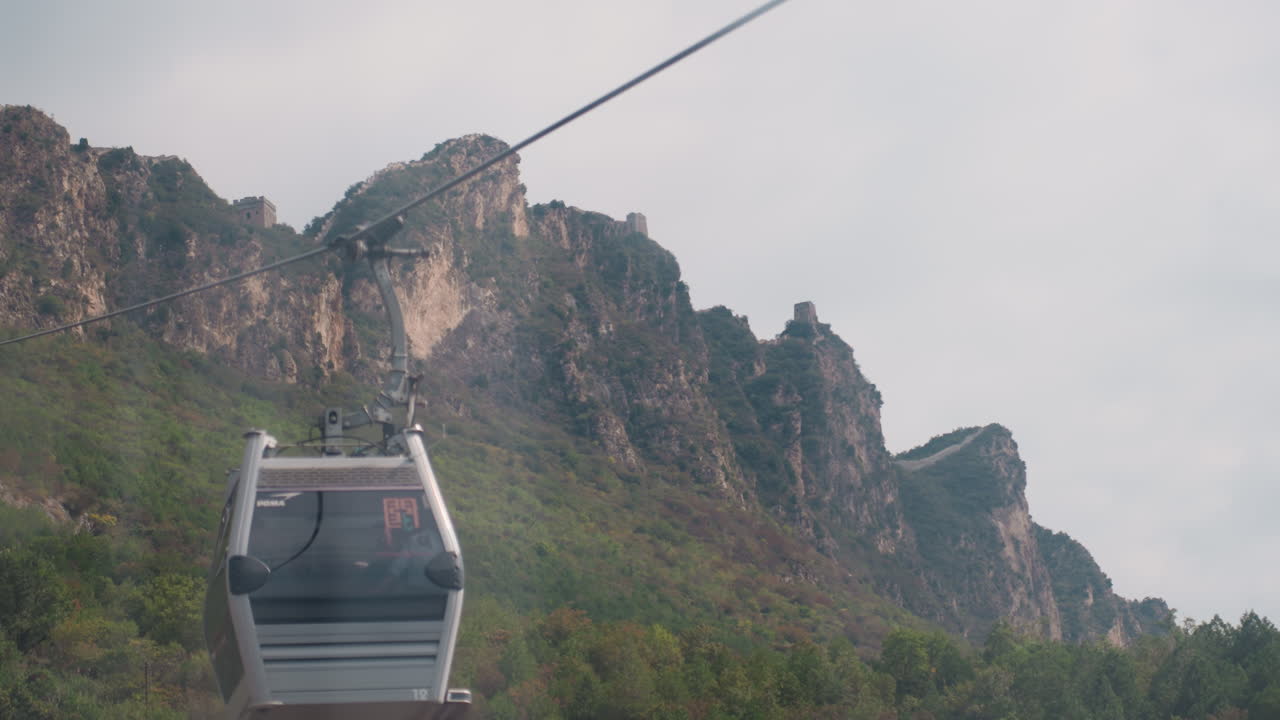La gondola si avvicina a cime montuose rocciose e frastagliate, un avventuriero sbircia attraverso il finestrino, un fotografo cattura la silhouette della vetta. La cabina oscilla delicatamente mentre le nuvole scivolano sui versanti calcarei, atmosfera epica.